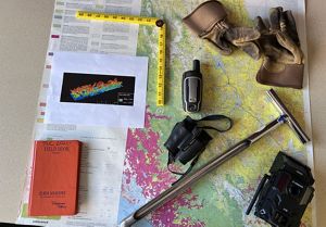 Items on a table for use in field conservation work, including a large map, gloves, a ruler, a notebook, a pair of binoculars, and a two-way radio.