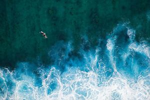 Aerial view of a surfer in a turbulent ocean escaping a massive wave crashing on the reef.
