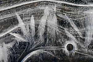 Wavy lines, scratches, and circular patterns decorate the surface of ice against a black background.