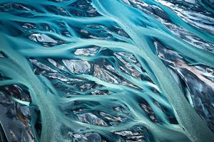 Aerial view of a glacier with networks of water moving through the ice, creating patterns that resemble veins.