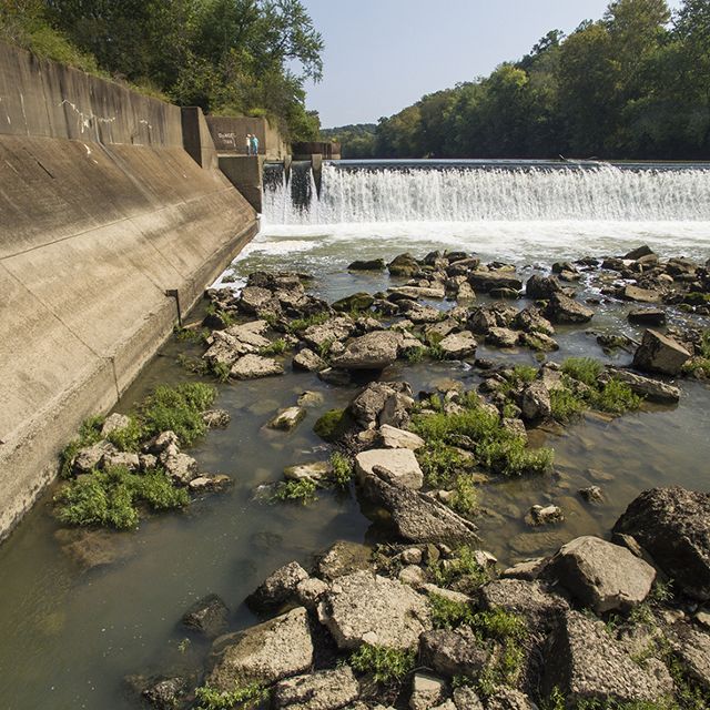 A rocky river with a large dam in the background.
