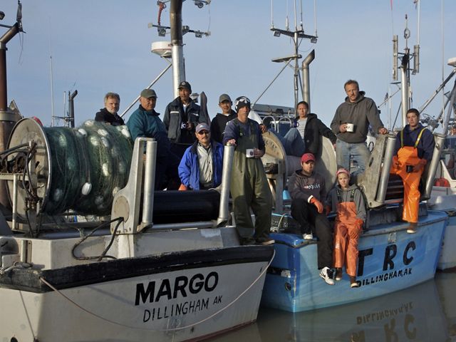 Several commercial salmon fishermen stand on the stern of one boat in a row of boats in Alaska's Bristol Bay.