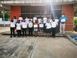 A group of children hold certificates outside of a schoolhouse.