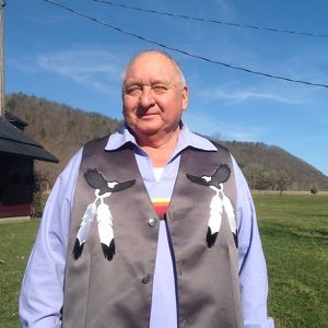 A mean wearing a gray vest with feathers hanging from it smiles for a photograph.