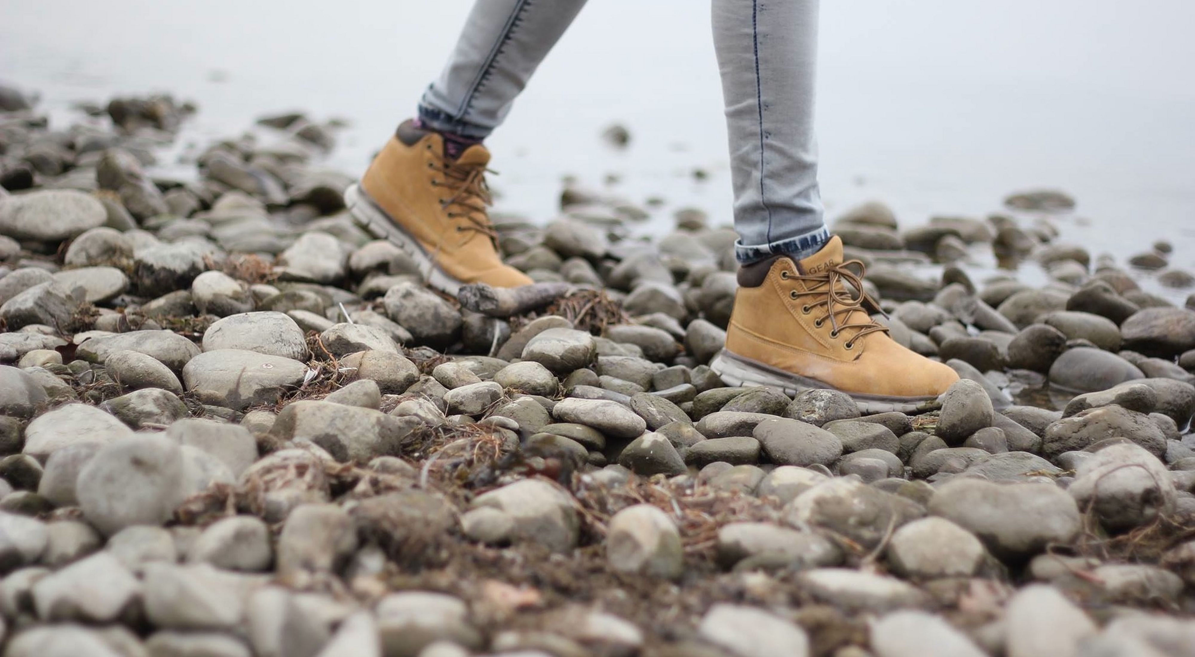 persons brown boots walking on gray pebbles