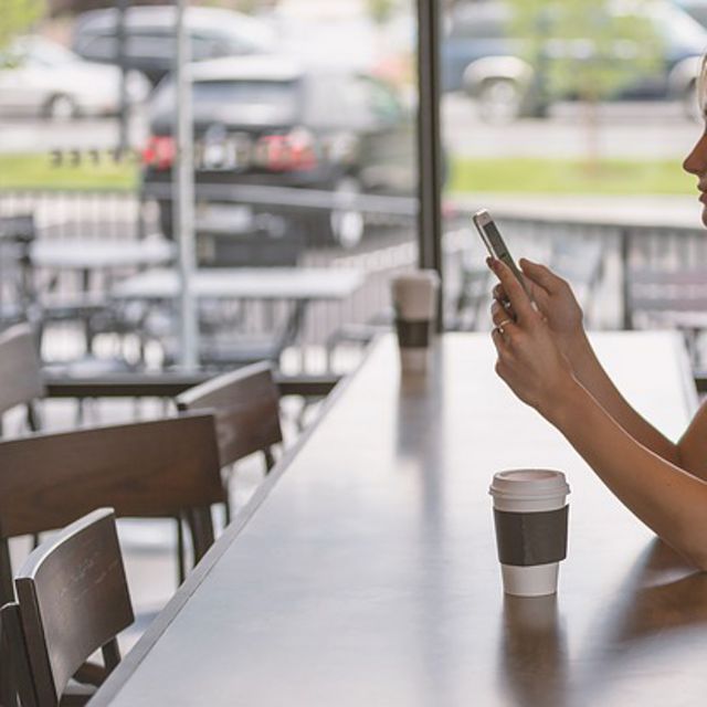 blond woman at empty coffee counter texting on phone