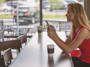 blond woman at empty coffee counter texting on phone
