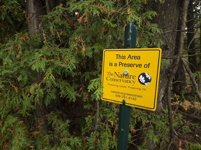 A sign in front of trees that says this area is a preserve of The Nature Conservancy. Protecting nature. Preserving life.  Nature dot org slash wisconsin. 