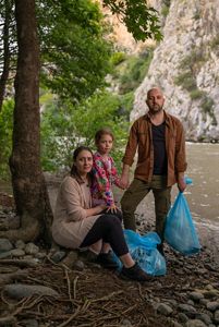 Andon Krstevski and his family hold blue garbage bags with the Vardar River behind them.