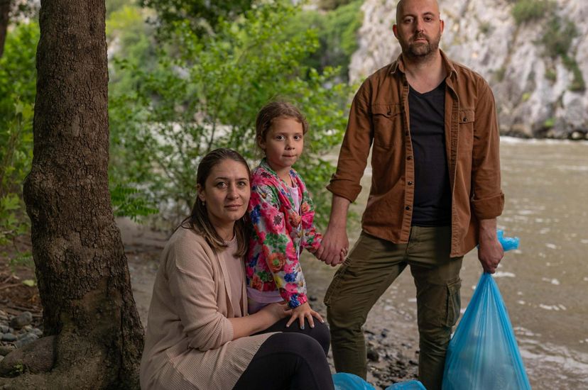 Andon Krstevski and his family hold blue garbage bags with the Vardar River behind them.