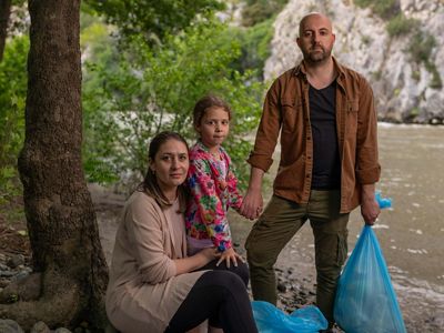 Andon Krstevski and his family hold blue garbage bags with the Vardar River behind them.