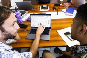 Two people look at a computer screen in a workshop environment.