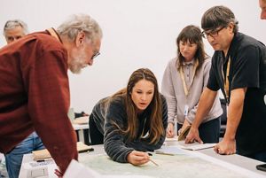 Symposium attendees leaning over a table. 