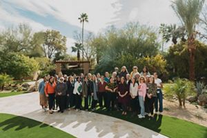 A group of women stand outside for a group photo on a sunny day. 