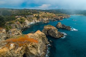 The deep blue water of the ocean meets the rugged, rocky terrain of the California coast.