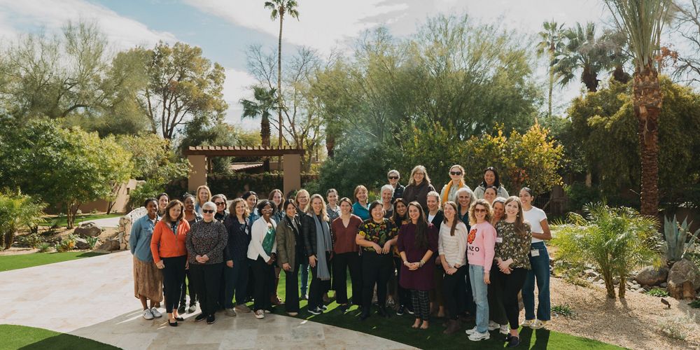 A group of women stand outside for a group photo on a sunny day.