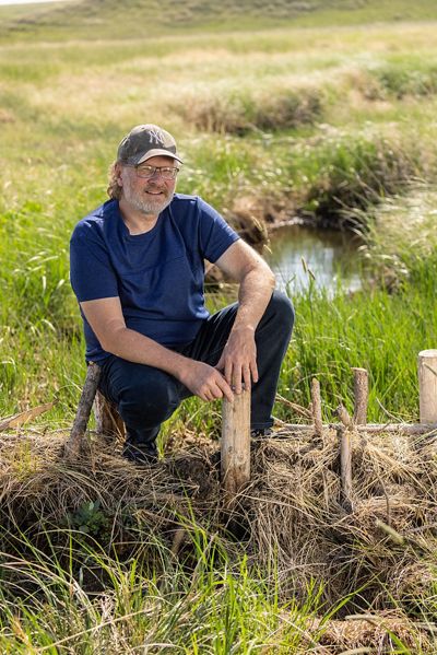 Markus Erk, a rancher, kneeling on top of a beaver dam analog installed along his stream.