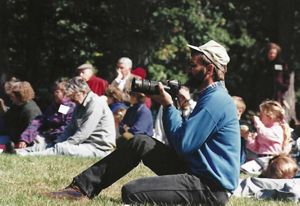 An old photo of a person sitting in a field holding a camera. 