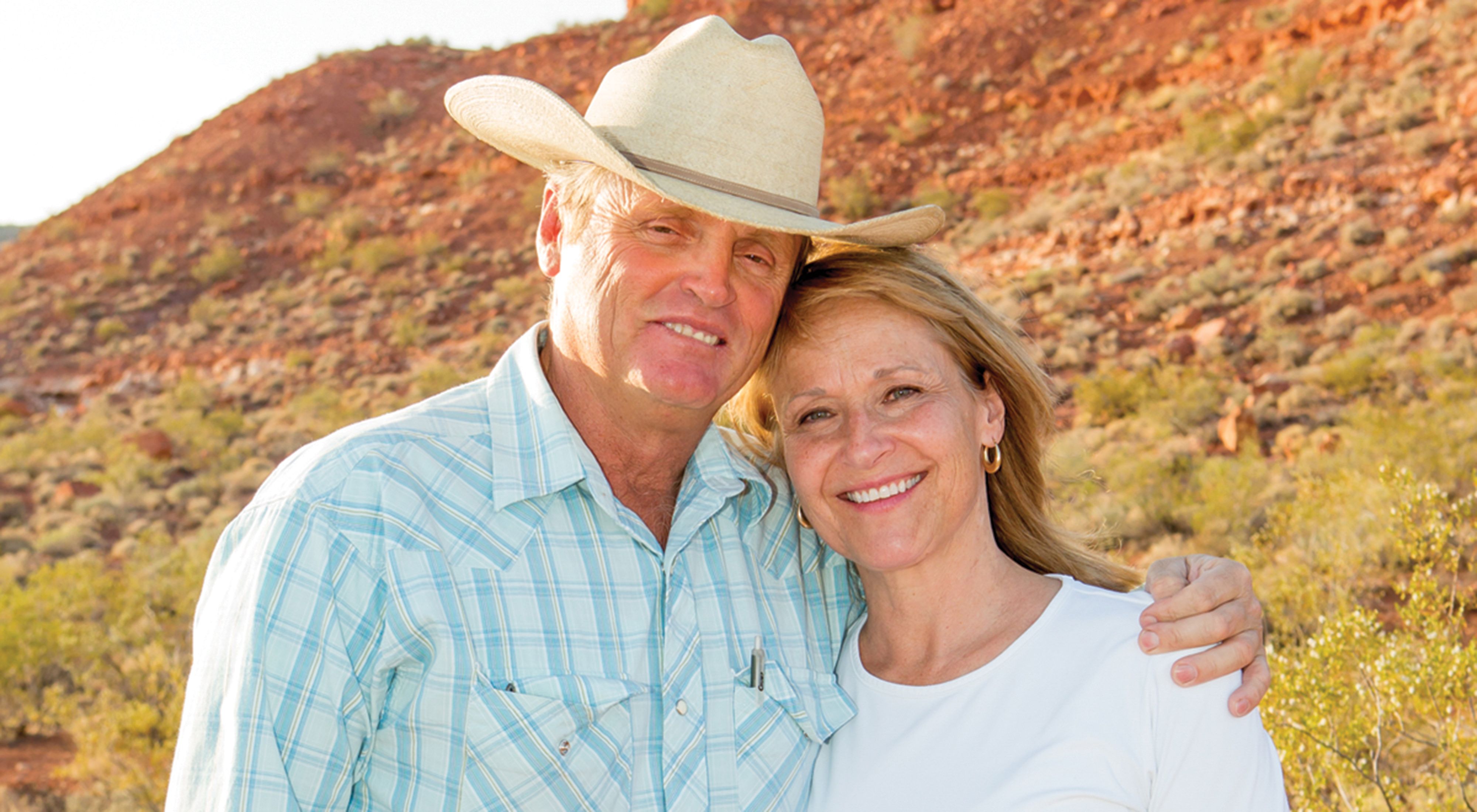 A smiling man in a cowboy hat poses with his arm around a woman who is also smiling. 