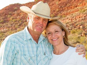A smiling man in a cowboy hat poses with his arm around a smiling woman. 
