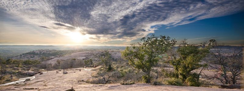 The sun sets over gleaming boulders dotted with shrubs.