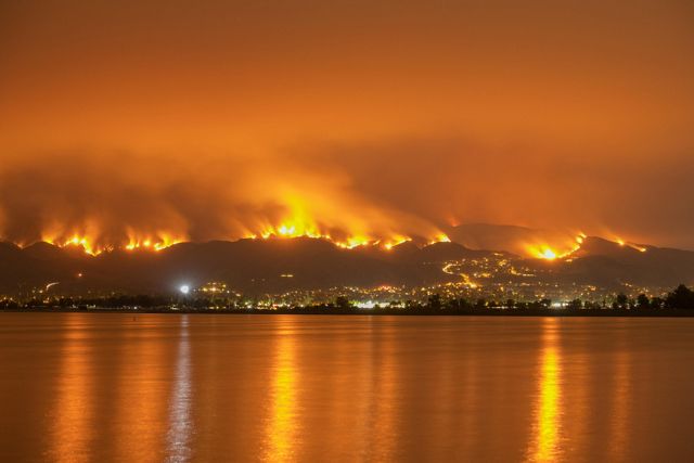 Photo of a wildfire in California, with orange flames reflecting off of the water.