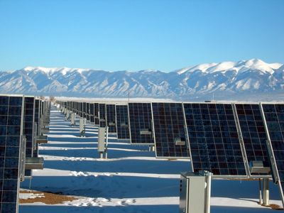 A field of solar panels sits at the base of a mountain range.