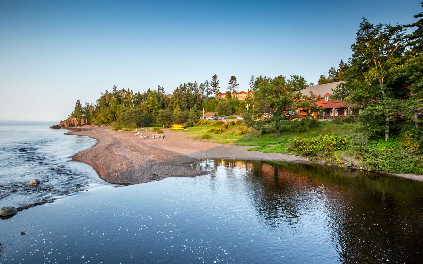 A lodge building is nestled amongst the green conifers along the shores of Lake Superior.