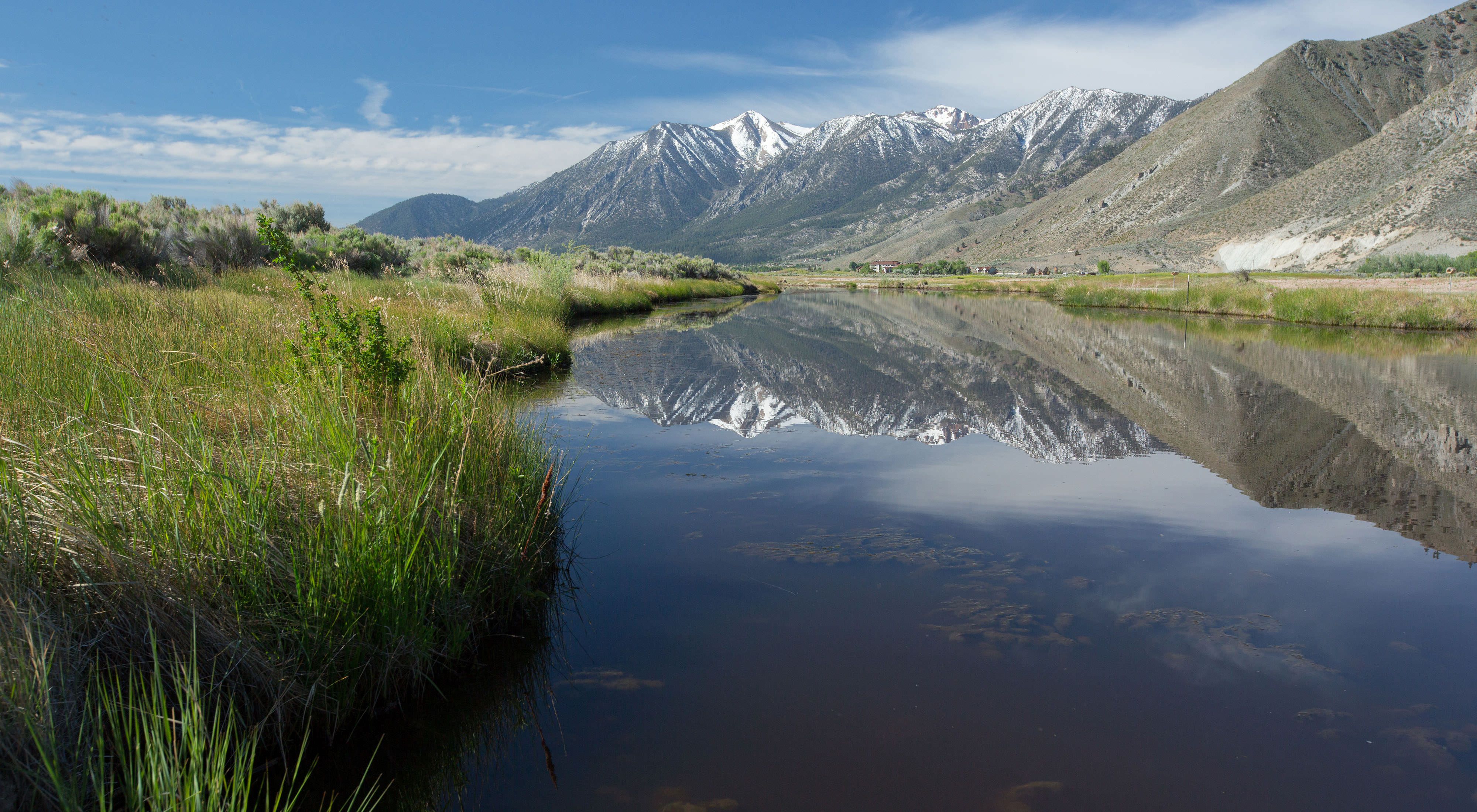 Snow-capped mountains reflected in the still water of the Carson River.