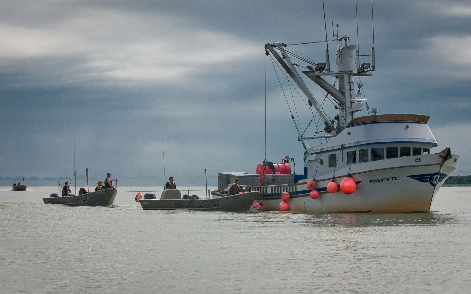 A large commercial fishing boat sits in a body of water with three smaller boats lining up beside it.