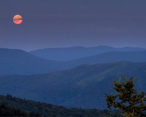 Blue mountains with orange sun in the background.