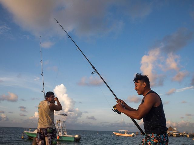 Dos hombres ríen mientras prueban suerte con sus cañas de pescar desde el muelle.