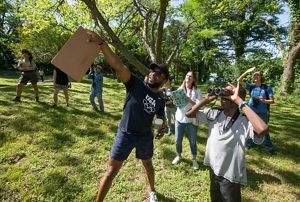 A group of people stand in a park and look to the left pointing. 