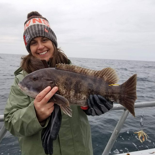 Virginia Fisheries Scientist Kate Wilke poses on a boat while holding a brown striped fish.