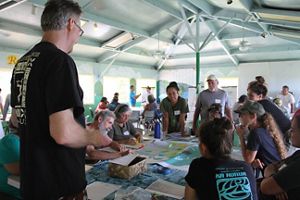 People gather around a table covered in maps. 