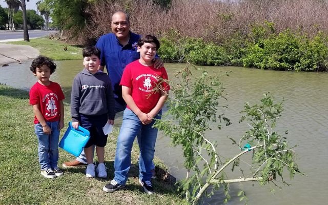 Tres niños pequeños están con su padre en la orilla de un río junto a un joven ciprés de Moctezuma que acaba de ser plantado.