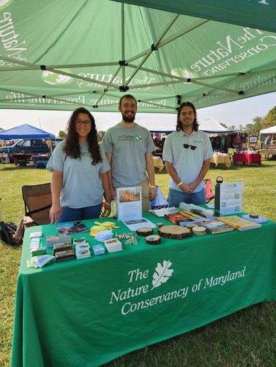Three TNC staff members stand behind a table covered with materials to share with patrons at a community event.