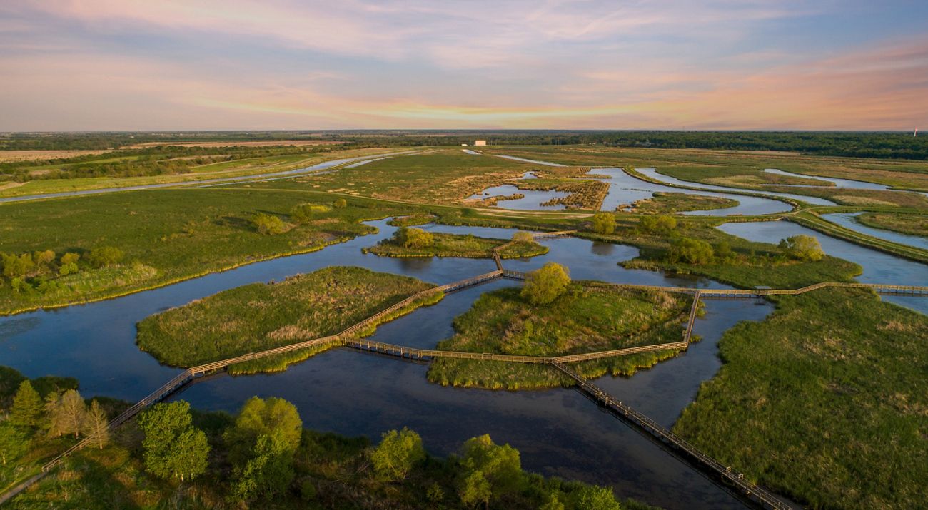 A mosaic of green wetlands and blue waters connected by wooden boardwalks.