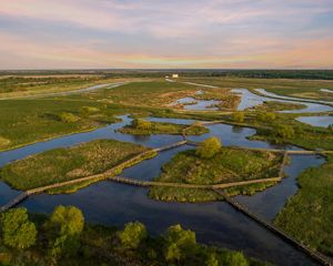 A mosaic of green wetlands and blue waters connected by wooden boardwalks.