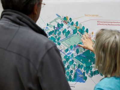 Two people stand in discussion in front of a board with colorful graphics.