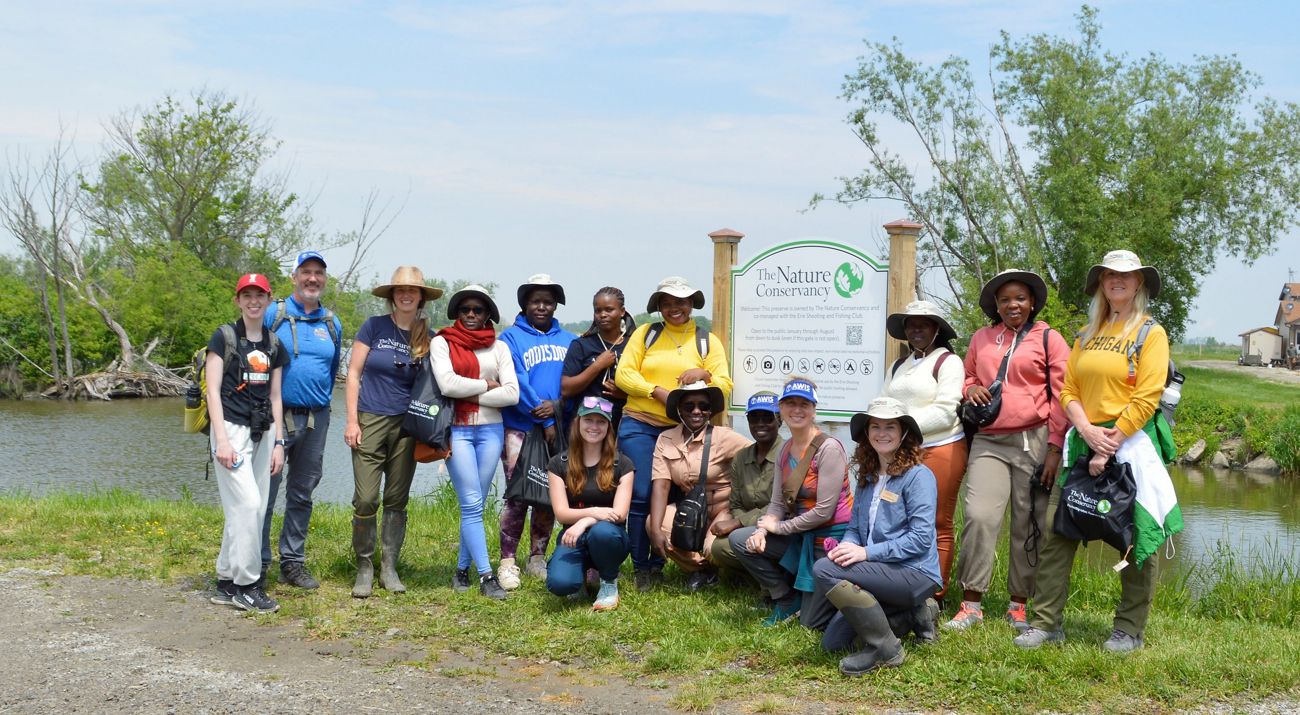 Group of people by a preserve kiosk sign on a sunny day.