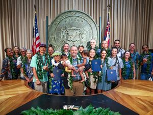 A group poses in front of a government seal. The man in the center holds an adorable baby in each arm. 