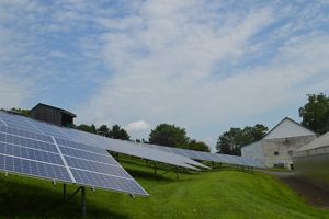 Solar panels on grassy foreground, barn in background.