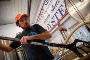 A man uses a long handled paddle to stir a mixture of water and longleaf pine branches and needles in a steel brewing tank.