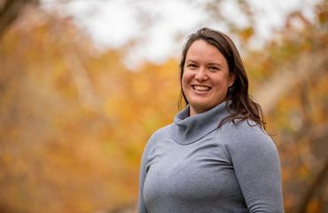 A smiling woman poses in front of some trees.