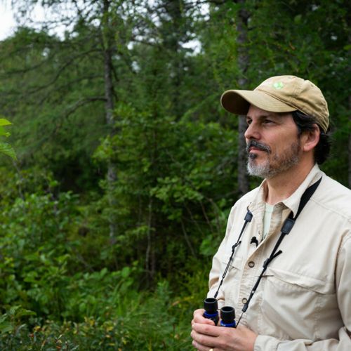 Jim Manolis holds binoculars in the forest.