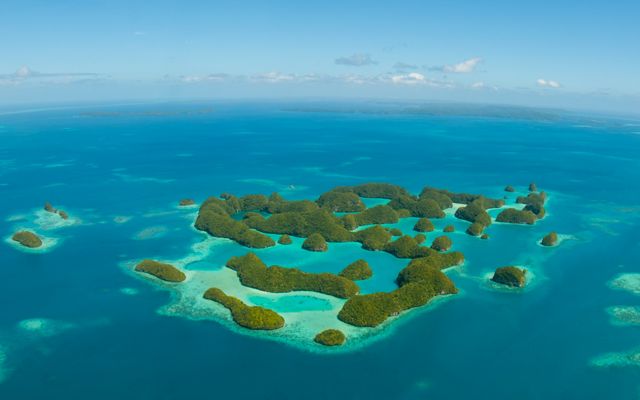 Aerial photo of tropical islands against a deep, blue sea, ringed by shallow coral reefs.