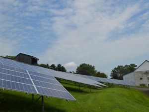 Solar panels on grassy foreground, barn in background.