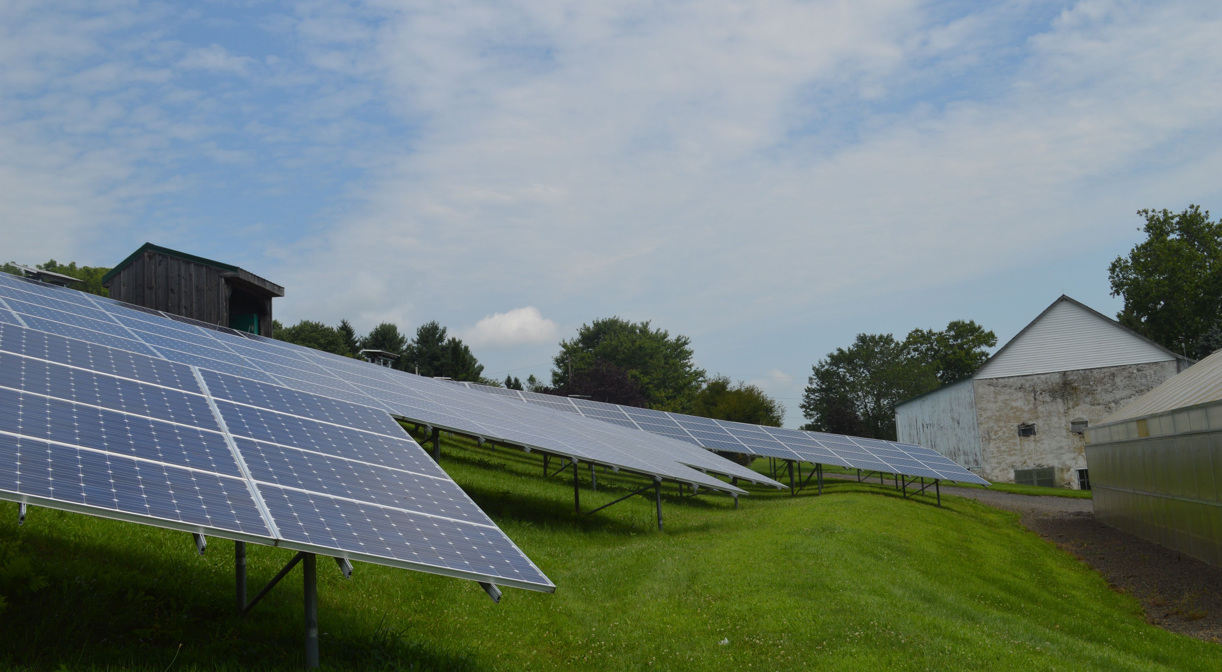Solar panels on grassy foreground, barn in background.