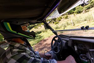 View from the interior of a small utility terrain vehicle of the driver behind the wheel wearing a protective helmet.